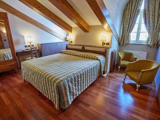 Comfortable bedroom with a striped blue and white bedspread, wooden beams on the ceiling, and a vintage armchair, offering a cozy atmosphere.